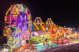 Illuminated Ferris wheel, bouncing castle and carousel at night in a funfair in Vientiane, Laos.jpg